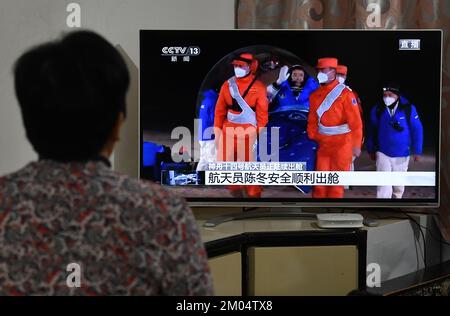 FUYANG, CHINA - DECEMBER 4, 2022 - Citizens watch a live TV broadcast of the re-entry module of the Shenzhou 14 manned spacecraft landing at Dongfeng Stock Photo