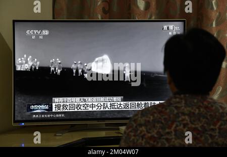 FUYANG, CHINA - DECEMBER 4, 2022 - Citizens watch a live TV broadcast of the re-entry module of the Shenzhou 14 manned spacecraft landing at Dongfeng Stock Photo