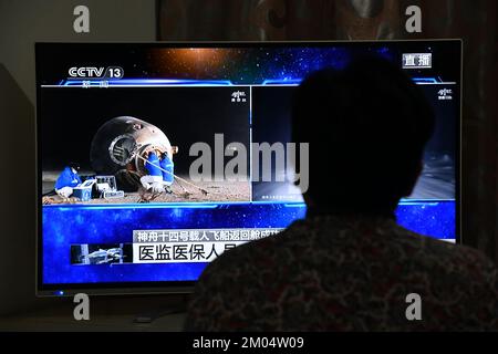 FUYANG, CHINA - DECEMBER 4, 2022 - Citizens watch a live TV broadcast of the re-entry module of the Shenzhou 14 manned spacecraft landing at Dongfeng Stock Photo