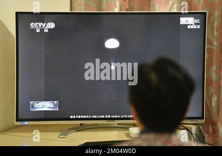 FUYANG, CHINA - DECEMBER 4, 2022 - Citizens watch a live TV broadcast of the re-entry module of the Shenzhou 14 manned spacecraft landing at Dongfeng Stock Photo