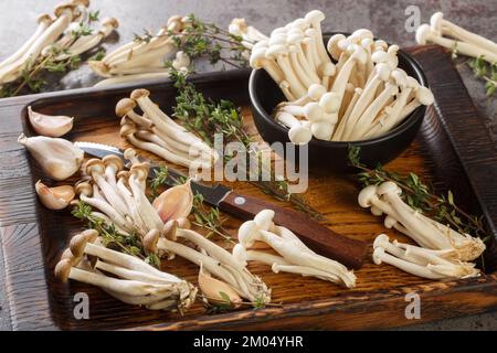 Fresh raw white and brown beech mushrooms with thyme and garlic on a kitchen cutting board on the table. horizontal Stock Photo