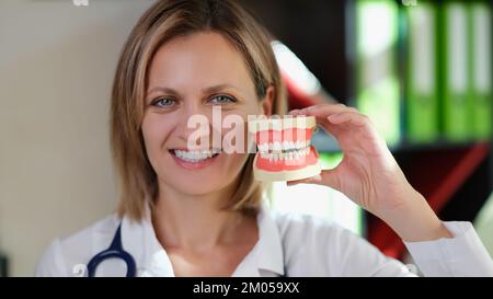 Female dentist smiling and shows artificial jaws in her hand closeup. Stock Photo