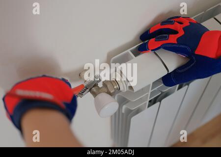 Gloved craftsman installs heating battery in house. Stock Photo