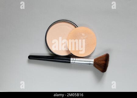 powder in a plastic round package and a brush on a gray background, women's cosmetics close-up, foundation powder Stock Photo