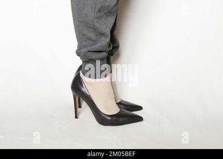 a young girl in gray sweatpants and black pointed toe high-heeled shoes stands on a white carpet at home Stock Photo