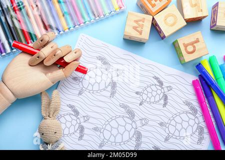 Coloring page, felt-tip pens, pencils, wooden hand and toys on blue background Stock Photo