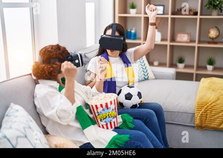 Two women mother and daughter watching soccer match using vr glasses at home Stock Photo