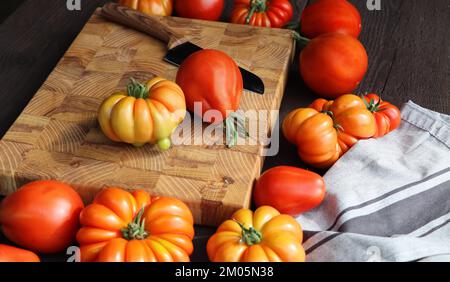 Fresh ripe hairloom tomatoes and knife on rustic wooden board over dark background Stock Photo
