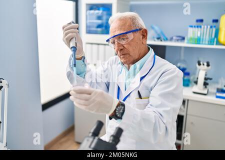 Senior man wearing scientist uniform using pipette working at laboratory Stock Photo