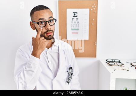African american optician man standing by eyesight test pointing to the eye watching you gesture, suspicious expression Stock Photo