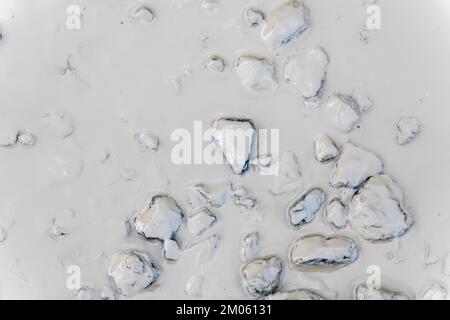 Submerged mud covered pebble / small stones in murky puddle on country track. For lack of clarity, as clear as mud idiom, mud slick. Stock Photo