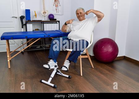 Senior caucasian man at physiotherapy clinic using pedal exerciser smiling cheerful showing and pointing with fingers teeth and mouth. dental health c Stock Photo