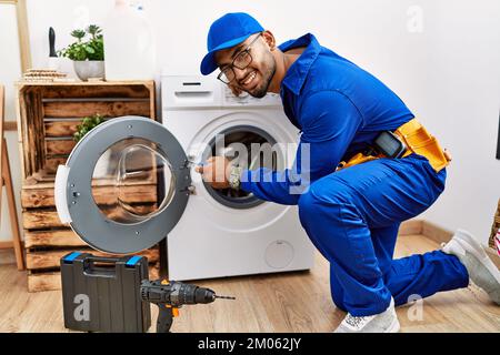Young arab man wearing technician uniform repairing washing machine at laundry room Stock Photo