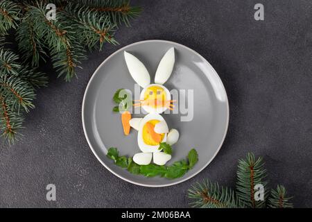 Funny rabbit made from boiled eggs, peeled carrots and arugula on gray plate. Creative food idea for kids, Top view Stock Photo