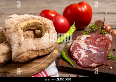 Serbian traditional homemade baked buns( lepinja), vegetable and cutting board with sliced prosciutto on wooden table. Selective focus. Stock Photo