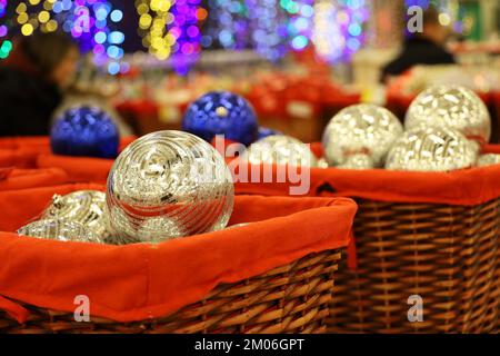 Christmas toys, golden and blue balls in red basket on blurred festive lights background. New Year decorations in a store Stock Photo