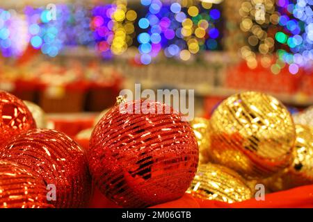 Christmas toys, red and golden balls in red basket on blurred festive lights background. New Year decorations in a store Stock Photo