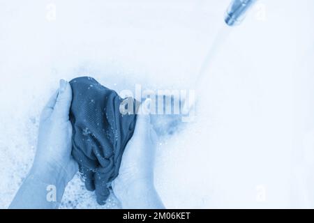 Female hands washing color clothes with running water in the sink Stock Photo