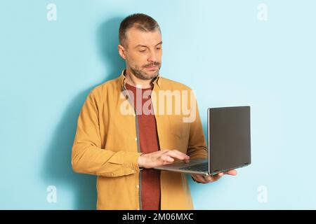 Smart businessman, employee working at computer. Serious mature man typing on laptop, standing on blue background Stock Photo