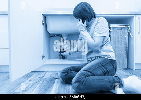 Woman with leaking sink in laundry room calling for help Stock Photo