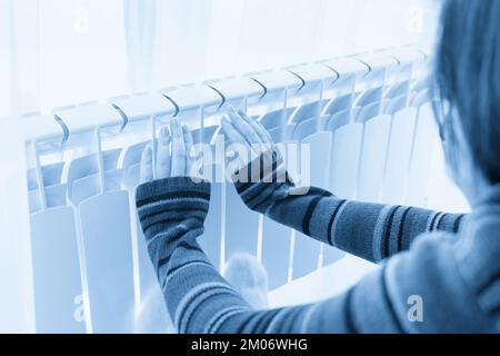 Girl warms up the frozen hands above hot radiator, close up view Stock Photo