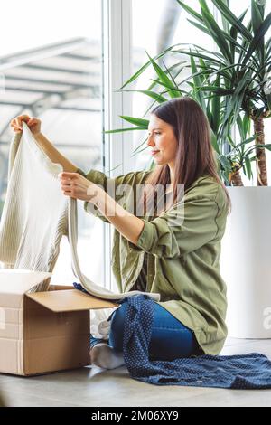 Vertical photo of a woman looking trough the clothes she bought online, taking them out of the box Stock Photo