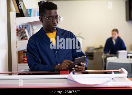 Attentive technical worker of printing house counts the cost of payment for work on calculator Stock Photo