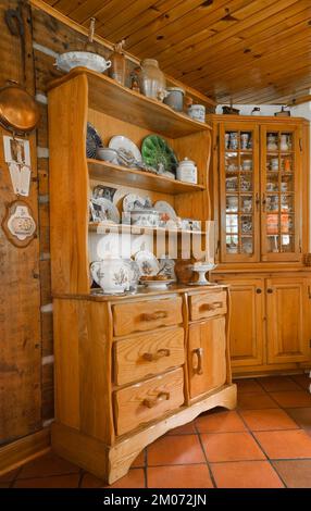 Antique buffets with assorted chinaware collection and curios in kitchen inside old 1800s reconstructed cottage style log home. Stock Photo