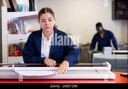 Work in printing house - woman cuts paper with professional cutter Stock Photo