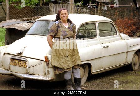 Prahova County, Romania, May 1990, a few months after the fall of communism- woman in the countryside leaning on an out of use automobile in her yard. Stock Photo