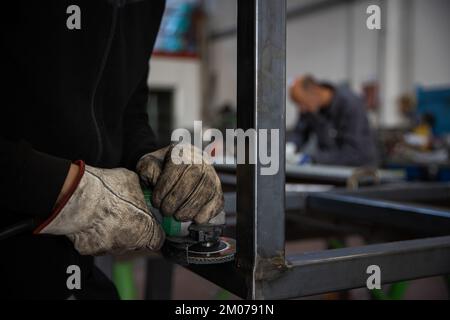 Close-up of the hands of a worker using the sander on a metal bar while wearing protective gloves Stock Photo