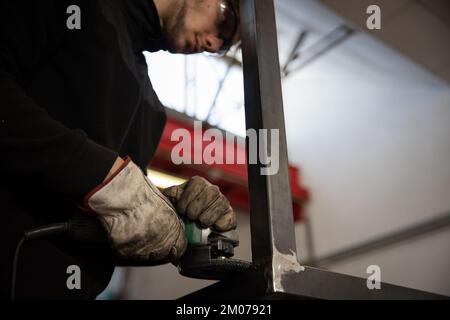 A worker uses a sander on a metal bar in a workshop Stock Photo