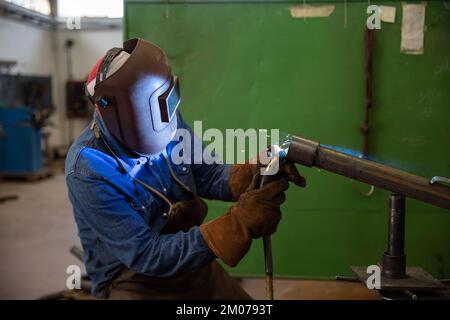 A welder welds a piece of metal in the factory, industrial work Stock Photo