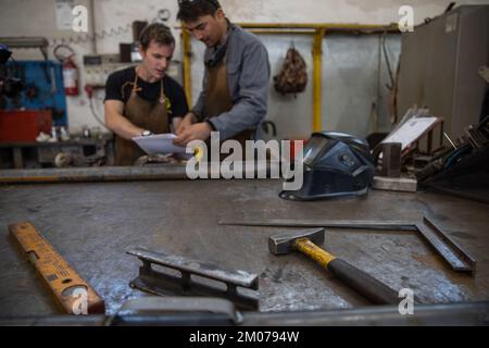 Two fellow workers look at the technical drawings in the factory, focus on working tools. Stock Photo