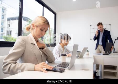 Young caucasian businesswoman using laptop computer and smart phone working at the office, woman and colleagues working with confident at workplace, s Stock Photo