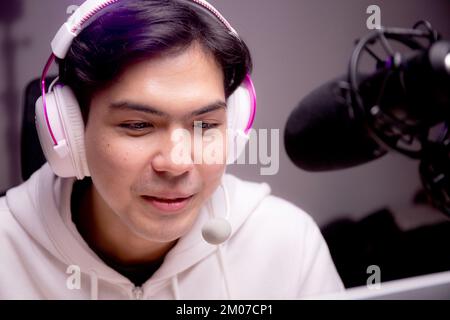 Young asian man for a podcast wearing headphones and speaking with mic in studio, host male or DJ wearing headset talking with microphone for entertai Stock Photo