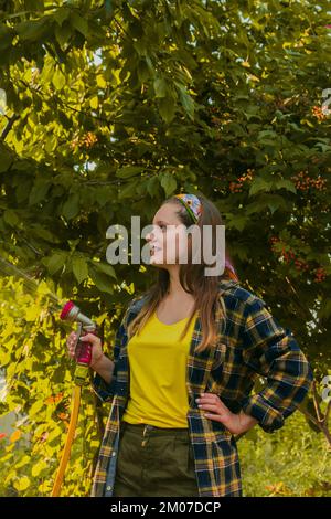 young pretty girl having fun in the garden watering plants with a hose. Smiling while taking a favorite hobby Stock Photo