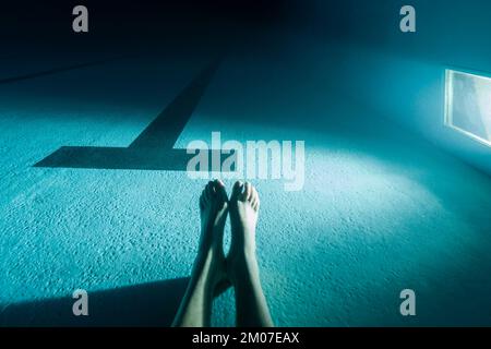 Two male feet lined up resting on the bottom of a swimming pool with a window coming in rays of light Stock Photo