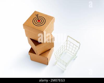Target icon on cardboard parcel boxes stack and empty shopping trolley cart on white background. Carton kraft paper box. Business marketing and delive Stock Photo