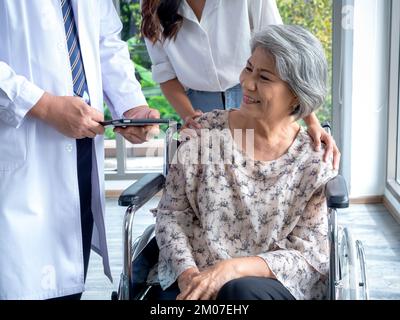 Portrait of smiling senior woman patients in wheelchair with assistant take her to meet doctor male use tablet discussing her medical treatment record Stock Photo