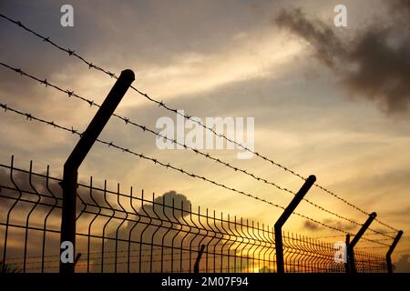 Barbed wire fence against twilight sky Feeling lonely and wanting freedom. Stock Photo