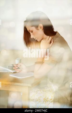 Jotting down her thoughts...Attractive young woman writing in her diary while in a coffee shop. Stock Photo