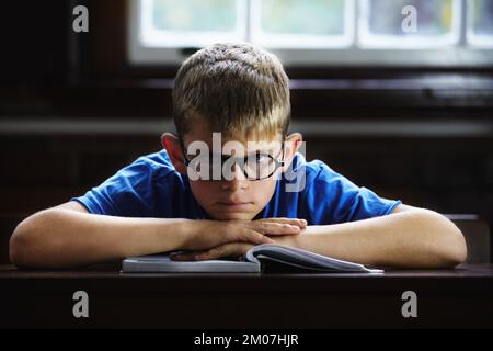 This work is boring. Young boy feeling overcome with boredom in the classroom. Stock Photo