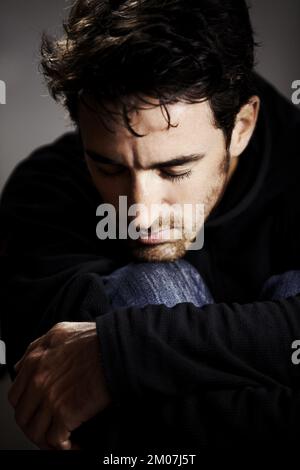 Hes feeling down. A young man resting his head on his knee with his eyes closed. Stock Photo
