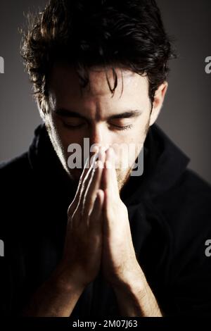Hes deep in prayer. A young man with his hands together and eyes closed in prayer. Stock Photo