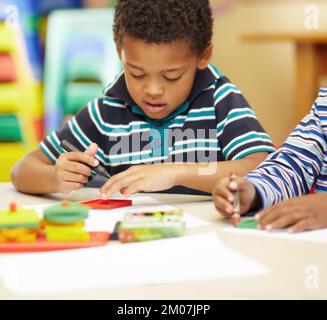Busy little hands. Two preschool african american boys concentrating on thier drawings with thier crayons and shapes- cropped. Stock Photo