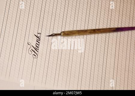 word thanks is written with a wooden ink pen on a white paper sheet with stripes drawn. stationery close up top view. spelling lessons and caligraphy Stock Photo
