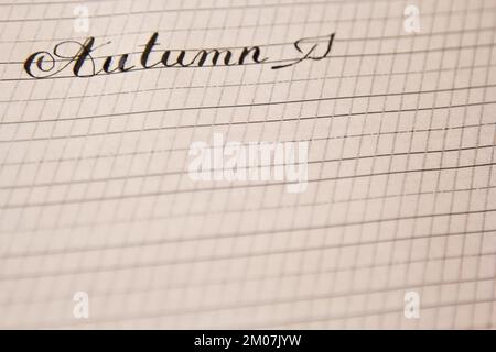 word autumn is written with an ink pen on a white paper sheet with stripes drawn. stationery close up top view. spelling lessons and caligraphy exerci Stock Photo
