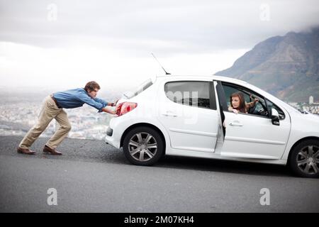 Just keep pushing...Young man pushing the car while his wife tries to start it - Vehicle breakdown. Stock Photo