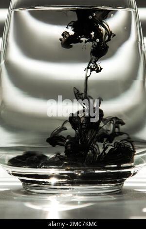 a cloud of ink in a transparent glass cup with clear water against the backdrop of a striped screen with rays of light. Template, layout, background, Stock Photo